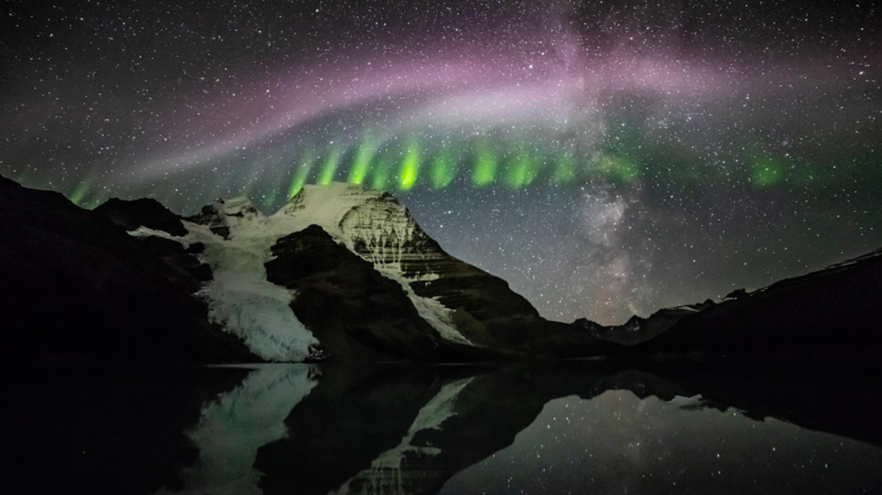 nighttime photo of mountain with pinkish swirls and green stripes and stars shining through