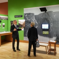 two people talk to each other in a gallery space with bright green walls and large black-and-white photos on the walls 