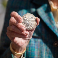 a photo of a hand extended outward and holding an Olympic gold medal from 1928 from Amsterdam 