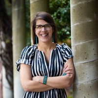 Tedde Simon, the new tribal liaison for UC Berkeley, wears a vertically-striped dress and turquoise jewelry and smiles while standing next to a pillar