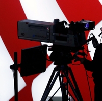 A television cameraman in silhouette against a U.S. flag suggests the deep importance of television advertising in political campaigns