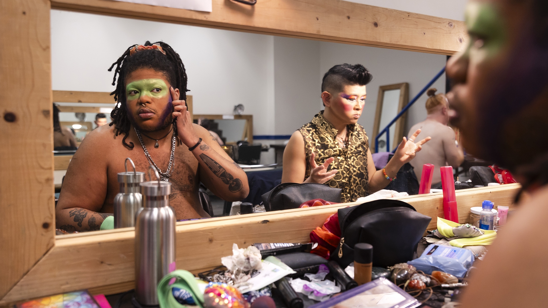 two people put their makeup on in a dressing room in front of a long mirror