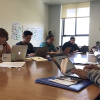 Teachers sit at a conference table using their laptops intently.