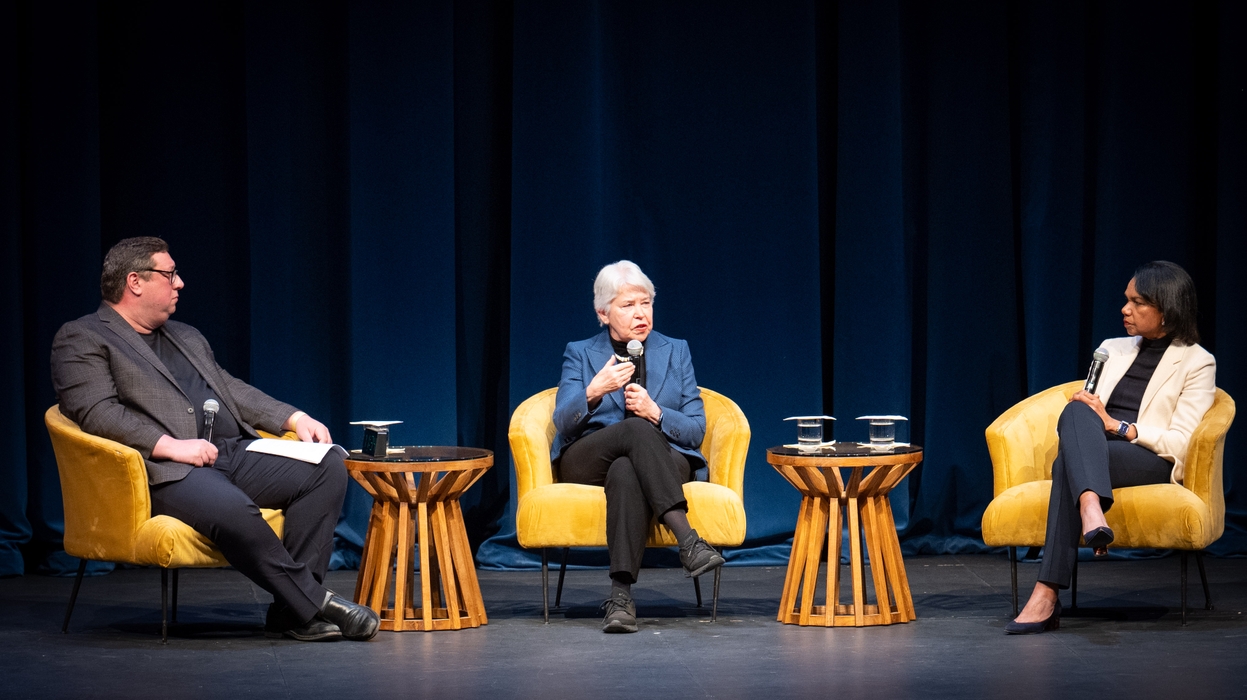 Three people seated on a stage holding microphones and speaking to an audience about the importance and challenges of protecting free speech.