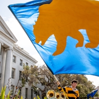 a person in the UC Berkeley rally committee waves a blue flag with a bear on it in celebration