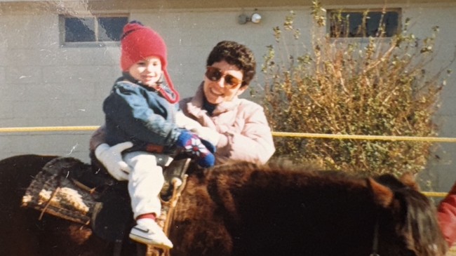 Justin Davidson as a toddler smiles as he rides a horse and his mom smiles and holds him on the saddle.