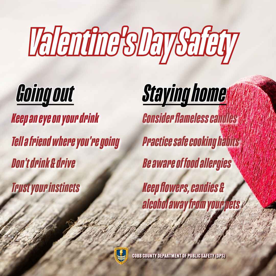 A Valentine's Day safety graphic from Cobb County Department of Public Safety. The image has a wooden background with a red heart on the right side. The title 'Valentine's Day Safety' is in bold red text. Two sections list safety tips: 'Going Out' includes keeping an eye on drinks, telling a friend, not drinking and driving, and trusting instincts. 'Staying Home' advises using flameless candles, practicing safe cooking, checking for food allergies, and keeping harmful items away from pets.