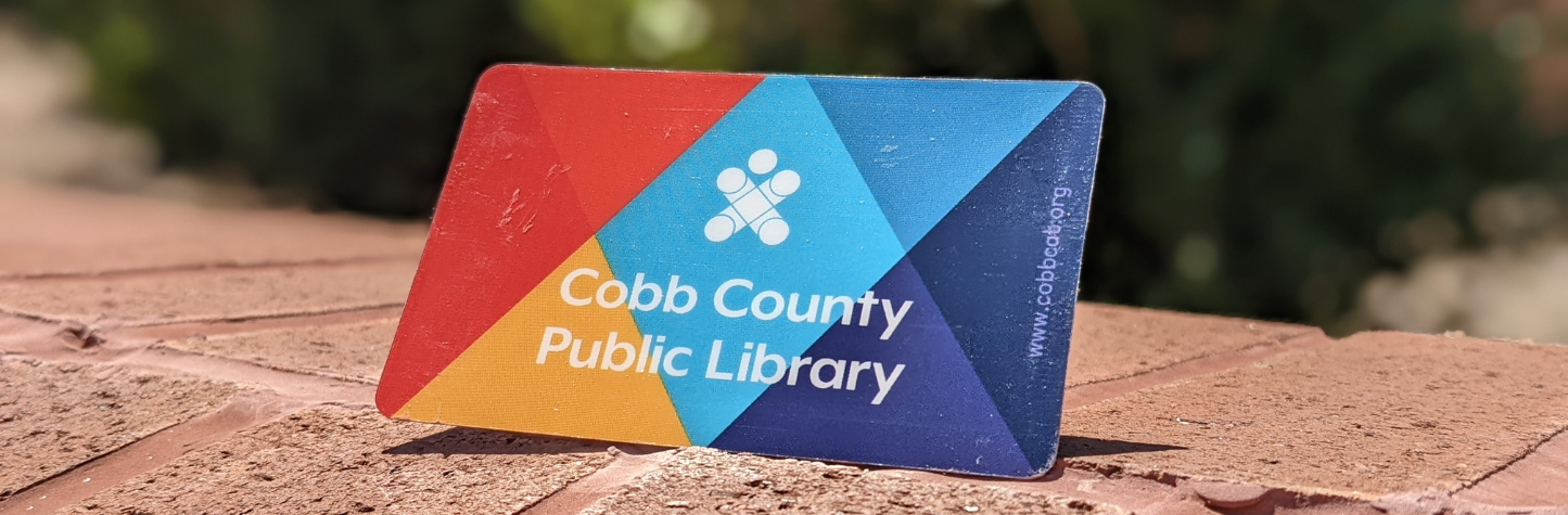 a Cobb County Public Library card on display on a brick ledge with greenery in the background