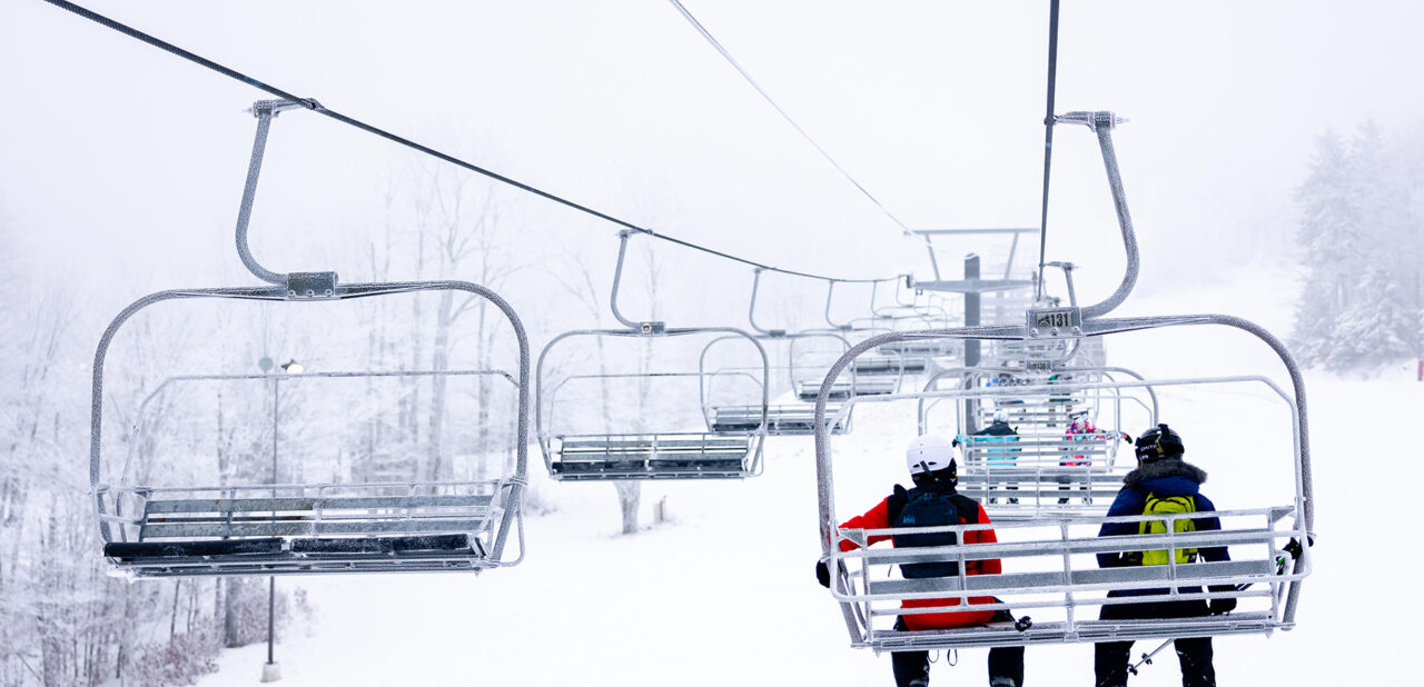 skiers on a ski lift heading up a snowy mountain