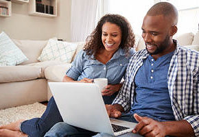Couple sitting on living room floor looking at laptop together