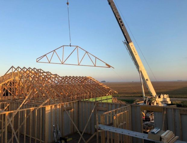 Photo of crane lifting roof truss to a house top