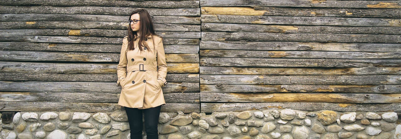 Woman in a trench coat leaning against a wall struggling with a past sexual assault