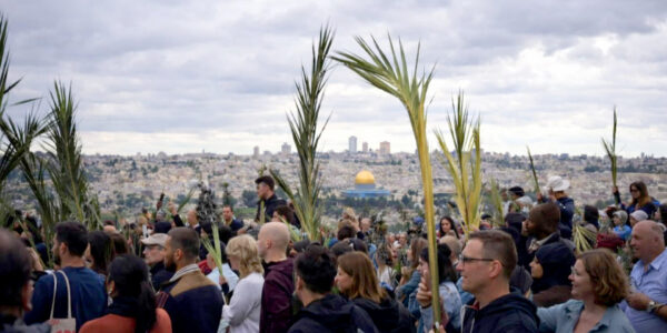 Procissão de Ramos em Jerusalém 2025. Pessoas com Ramos, ao fundo da imagem a cidade velha de Jerusalém. 