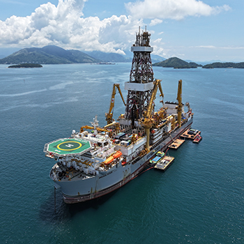 Vista aérea de plataforma de perfuração offshore, com helicóptero na área de heliponto, em mar aberto, destacando as operações no setor de petróleo e gás.