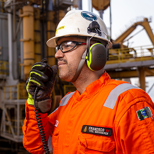 Close-up profile of a worker wearing a helmet and ear protectors, speaking into a black walkie-talkie.