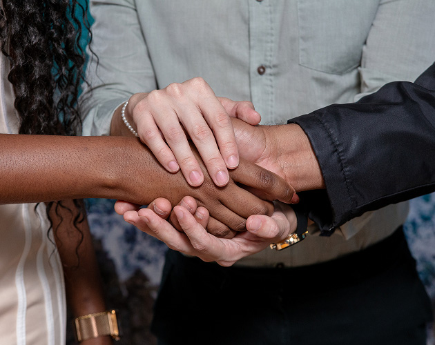 Close-up of four hands of people of different skin tones, stacked and intertwined over each other, symbolizing unity, diversity, and mutual support