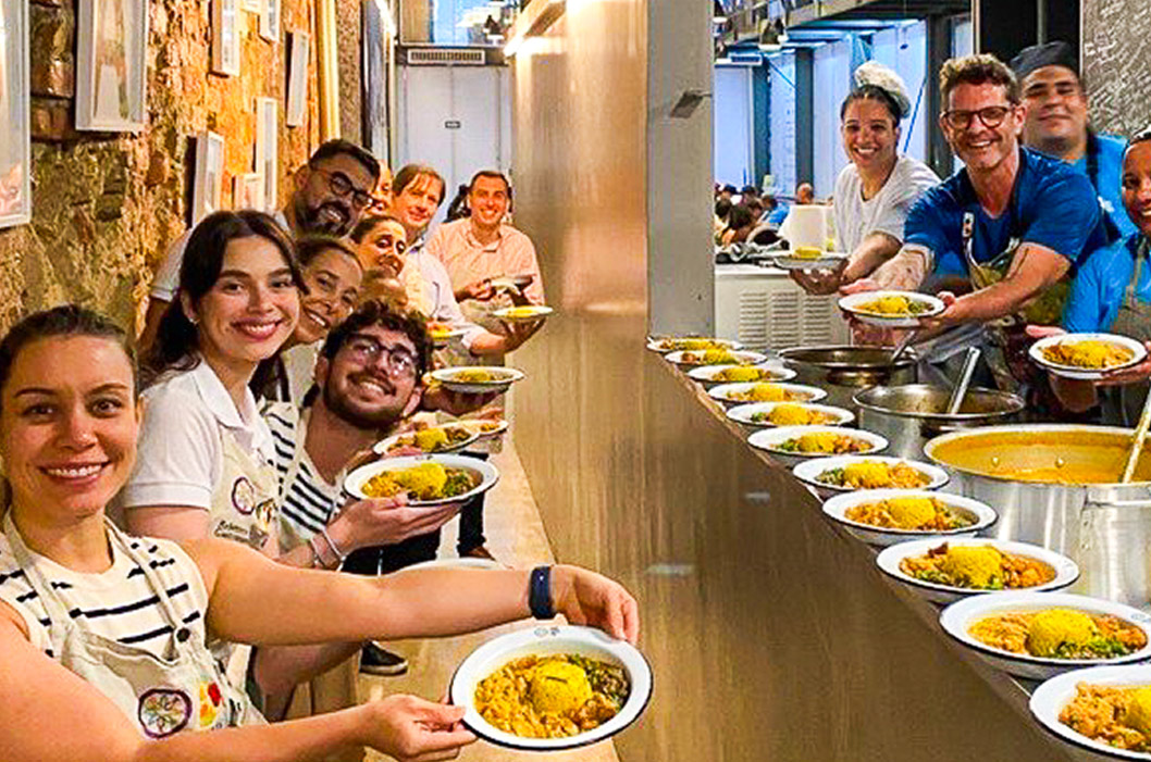 Team of volunteers smiling while holding plates of food in a distribution line.