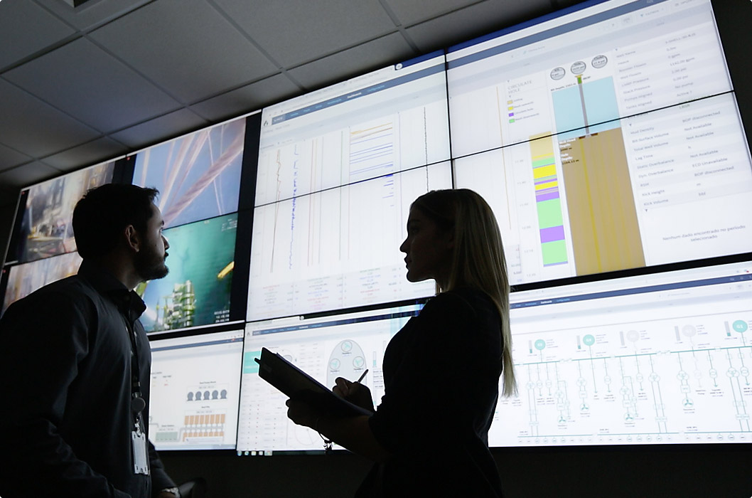 People talking in a monitoring center with multiple control and data screens.