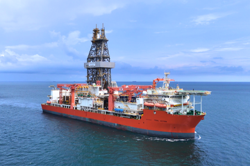 Drillship with a red and white hull, identified as 'Tidal Action', sailing in blue waters under a clear sky with scattered clouds