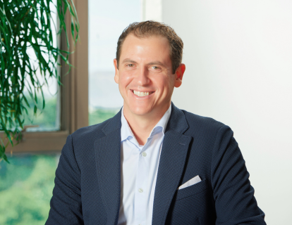 Profile photo of Daniel Rachman, a white man smiling, wearing a navy blue blazer and a light blue dress shirt without a tie.