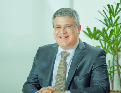 Profile photo of Leonardo Guimarães, a white man with glasses, smiling, wearing a gray suit, white shirt and golden tie