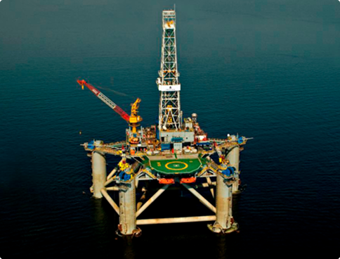 Aerial view of the 'Atlantic Star' semi-submersible rig in operation at sea. The platform has a deck with a prominent green helideck, a red crane, and a centrally located white derrick.