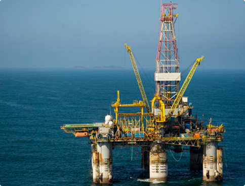 The 'Olinda Star' semi-submersible platform seen from a distance in a calm blue sea. The structure has large flotation columns, yellow cranes and a tall derrick with red and white latticework.