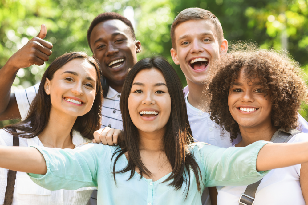 Group of multi-ethnic teen friends taking self portrait picture outdoors and sincerely smiling at camera