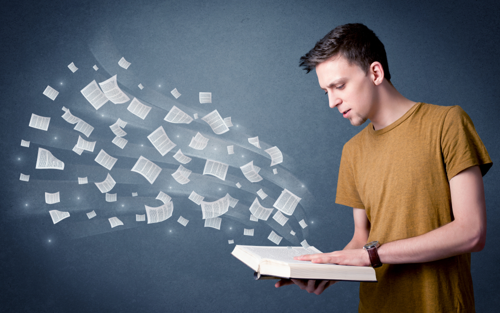 young man reading a book with pages flying from it