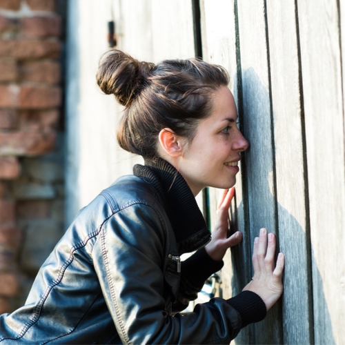woman spying through a hole in the fence