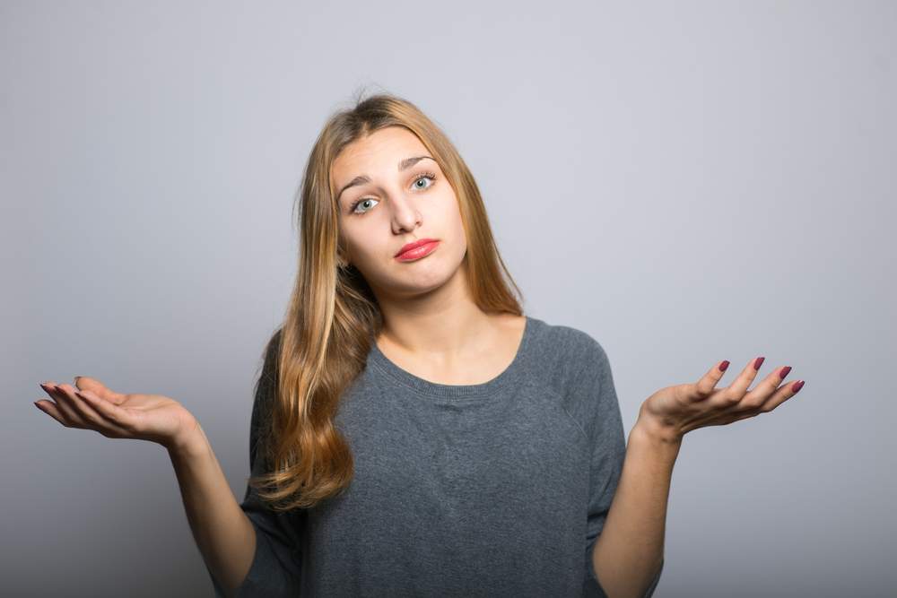 young woman looking confused while shrugging her shoulders