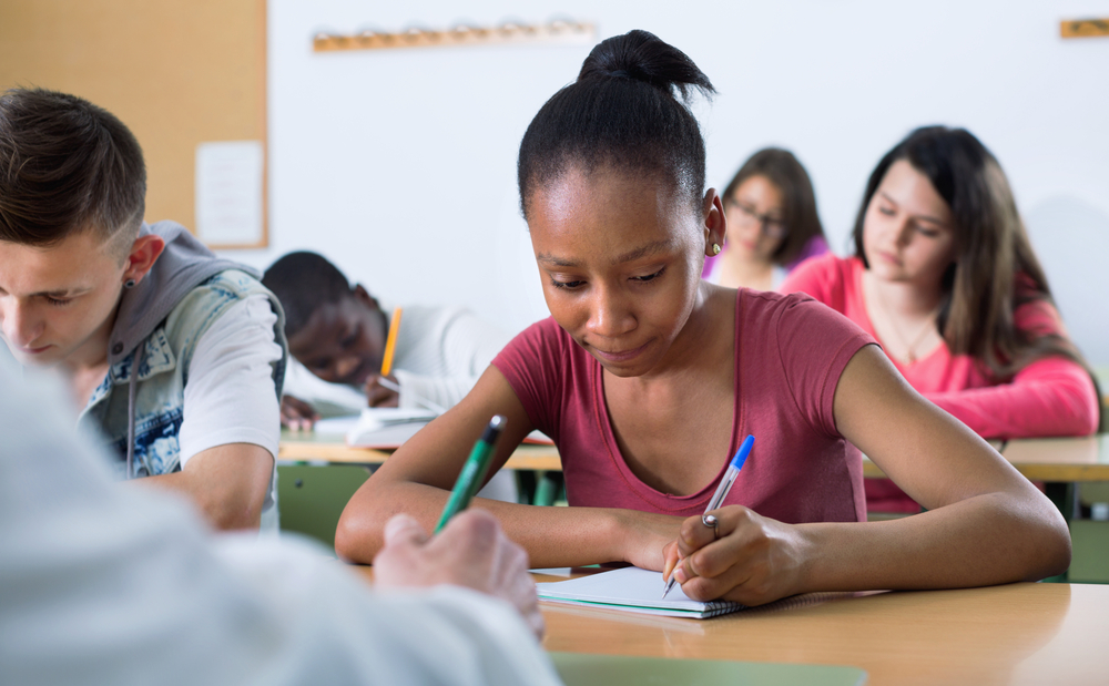 young girl writing on a notebook, in a class room