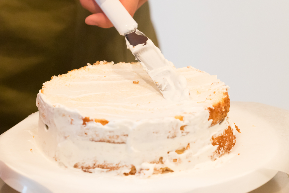 white layer cake being frosted with vanilla frosting