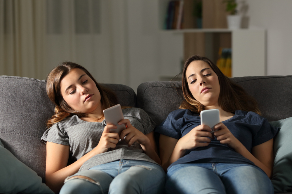 couple of girls sitting on couch looking at their phones