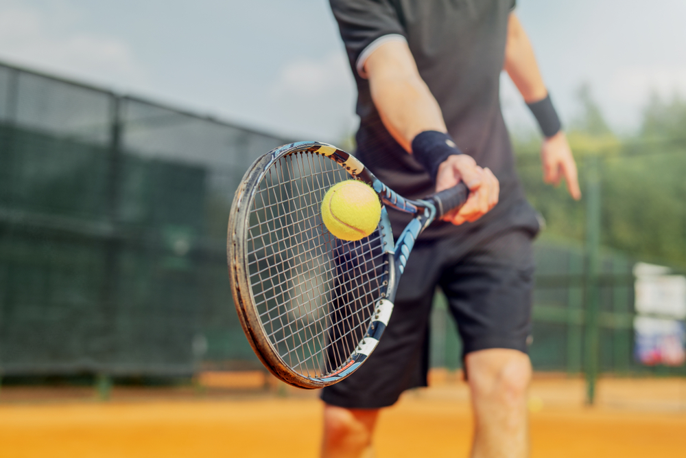man swinging tennis racket at ball