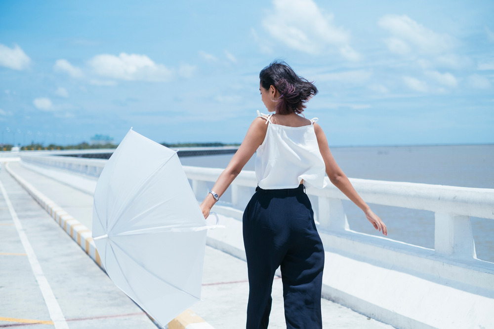 Person holding a white umbrella while walking on a sea bridge on a windy day.