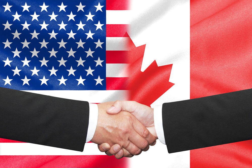 two businessman having a handshake over us and canada flag