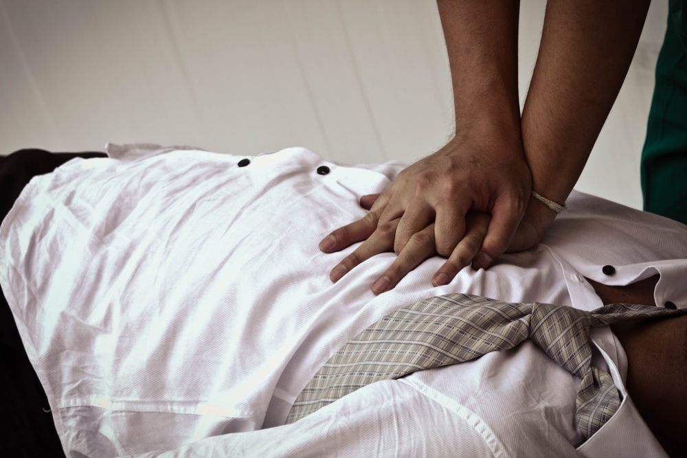 two hands doing chest compressions on a person wearing white shirt and tie