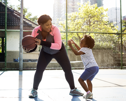 mom and young daughter laughing outside while playing basketball