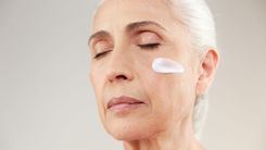 Na prevenção da ceratose actínica, é fundamental proteger a pele contra os danos provocados pela radiação ultravioleta (UV). A aplicação regular de protetor solar é uma medida essencial, pois auxilia no bloqueio dos raios UV. Mulher mais velha com um pouco de protetor solar no rosto.