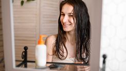 A hidratação pode ser feita de várias formas, basta escolher os produtos que se adequam às suas necessidades. Mulher com os cabelos molhados se olhando no espelho, com um creme em sua frente.