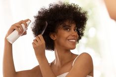 Os cuidados capilares envolvem tratamentos que vão desde o couro cabeludo até as pontas. Mulher passando um creme e penteando seus cabelos em frente a um espelho.