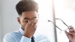 Tremedeiras nas pálpebras pode acontecer com todo mundo e normalmente é causado por estresse. Homem de roupa social com as mãos nos olhos.