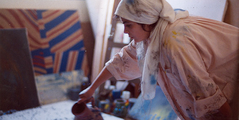 a girl with a covered head stands in a room filled with artwork