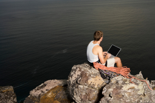 male using laptop near lake