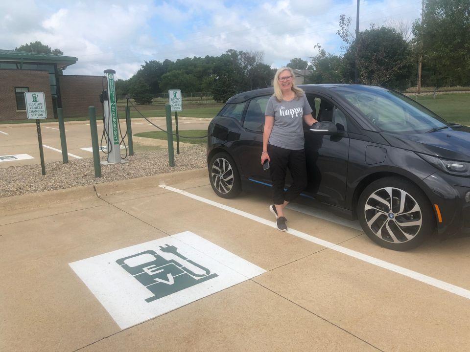 Customer standing by car while she uses Iowa Lakes charging station to charge her electric vehicle