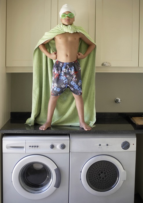 boy in cape on top of washer and dryer