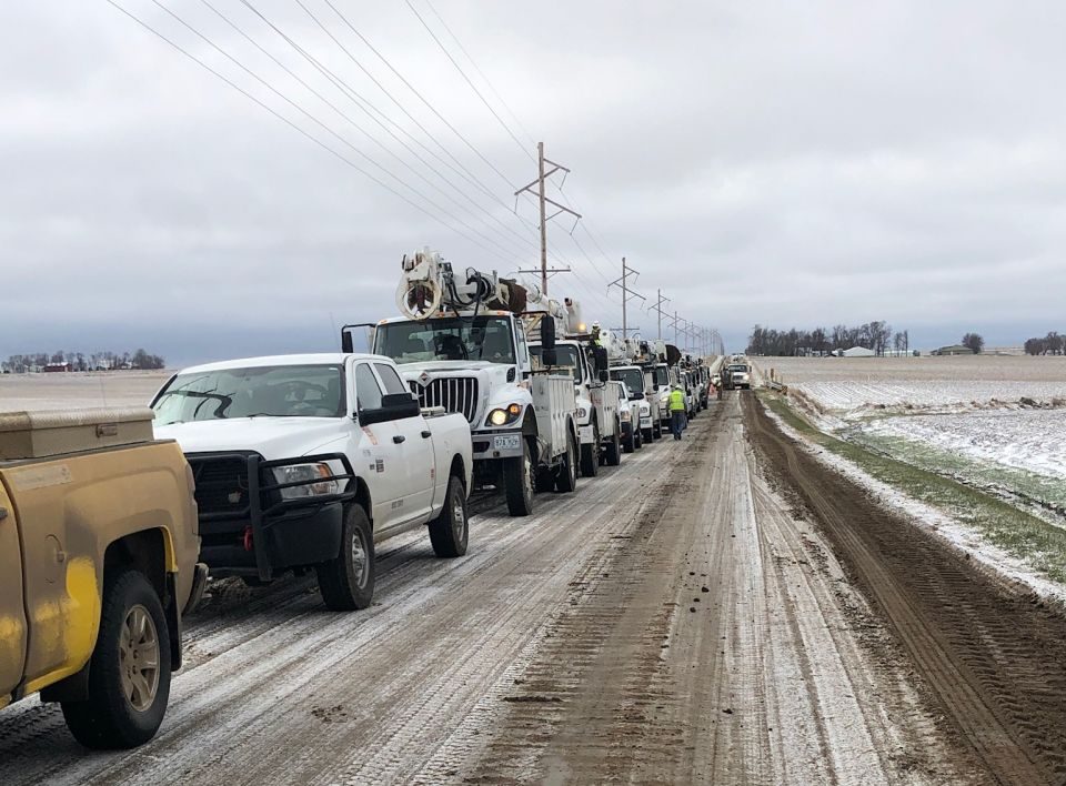 Several work trucks line up on the side of the road as line worker crews repair the damaged electric infrastructure
