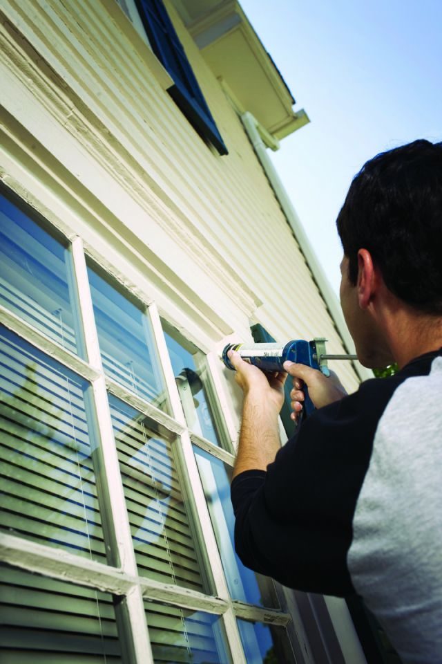 male homeowner caulking around a window