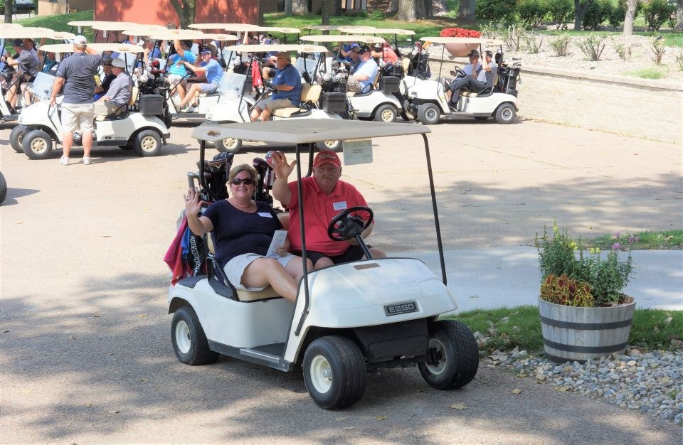 Two golfers wave, while riding in a golf cart